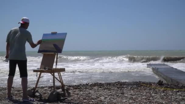 Artista pintor de tormentas marinas con un caballete en la playa pintura de la orilla del mar tormenta del océano viento olas sol cielo agua horizonte panorama pintura pincel creación obra maestra pintura paisaje pintor maestro — Vídeo de stock