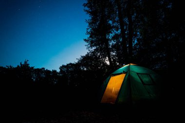 Yıldızlı bir akşamın altında, ormanda parlayan mavi bir çadır..