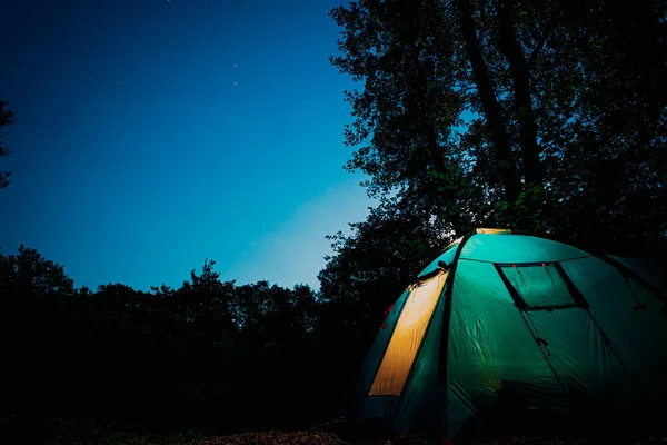 Świecący niebieski namiot w lesie pod gwiaździstym wieczornym niebem. — Zdjęcie stockowe