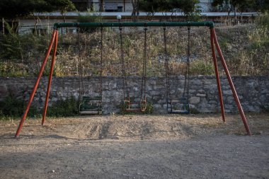 Çocuklar oyun alanında zincirle sallanıyor.