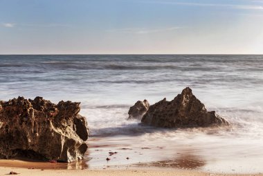 A erosao fragmenta a rocha em pequenos graos de areia e vai deixando para tras partes de rocha no meio do areal e na zona de rebento das ondas, o que produz lindas fotografias, fotografia tirada na Praia da Ilha em Porto Covo, Portekiz, Europa