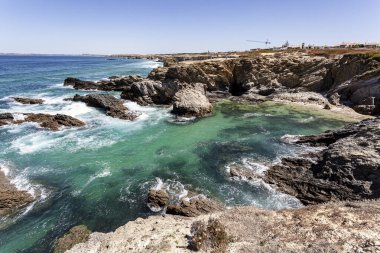 Portekiz Alentejo 'daki kayalıklar tarafından deniz dalgalarından korunan şeffaf koy.