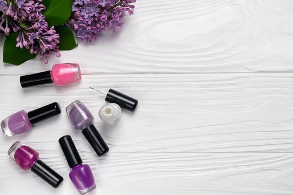 Bottles of nail polish on white wooden background with spring flowers top view with space for text