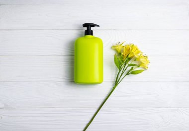 Şampuan veya duş jeli yeşil şişe beyaz ahşap arka plan üzerinde çiçek ile