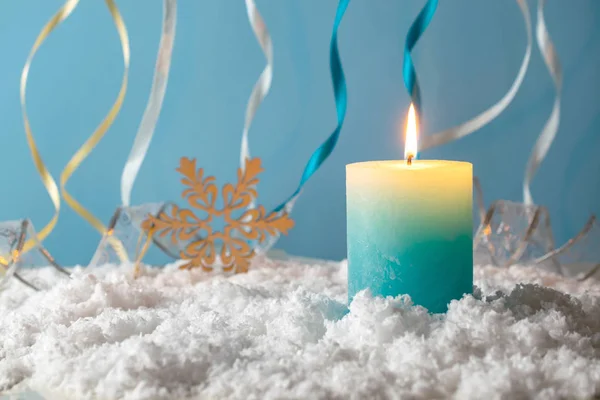 Blue and yellow burning christmas candle in the snow agains blue background — Stock Photo, Image