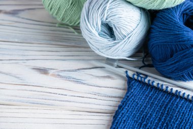 Mavi ve yeşil iplikli örgü kompozisyonu ve beyaz ahşap arka planda iğneler.