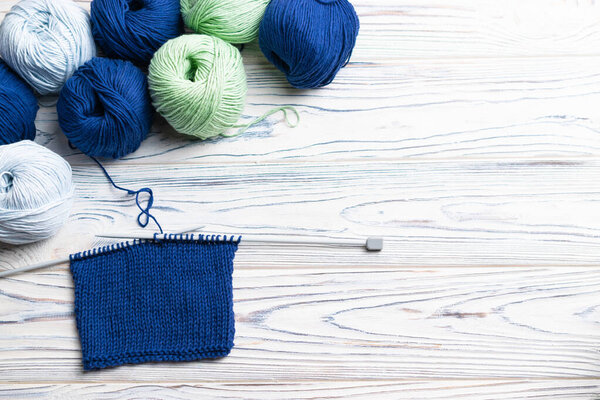 Knitting in progress. Flat lay composition with blue and green yarn and needles on white wooden background.