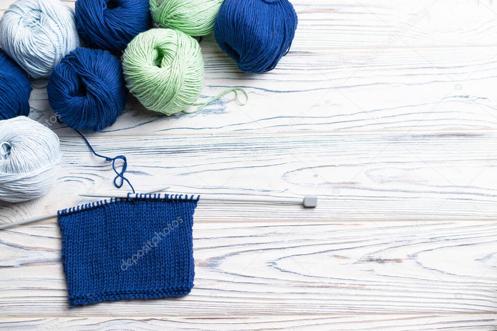 Knitting in progress. Flat lay composition with blue and green yarn and needles on white wooden background.