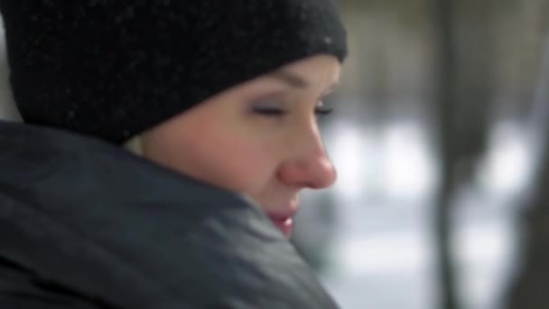 Joven chica feliz con abrigo de piel negra soplando en la nieve en el Parque. Vacaciones de invierno. Retrato de chica feliz en el parque de invierno, ella juega con la nieve . — Vídeos de Stock