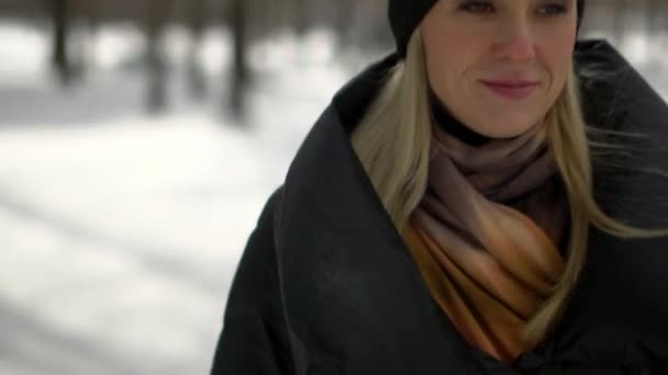 公園で雪の上を吹く黒い毛皮のコートで若い幸せな女の子。冬の休暇。冬の公園で幸せな女の子の肖像画、彼女は雪で遊ぶ. — ストック動画