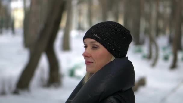 Jeune fille heureuse en manteau de fourrure noire soufflant sur la neige dans le parc. Vacances d'hiver. Portrait de fille heureuse dans le parc d'hiver, elle joue avec la neige . — Video