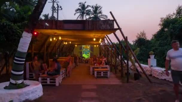 Bar restaurante junto a la playa iluminado por antorchas en llamas, al atardecer en Goa tropical. Idílica noche romántica de verano cenando bajo un cielo púrpura . — Vídeos de Stock