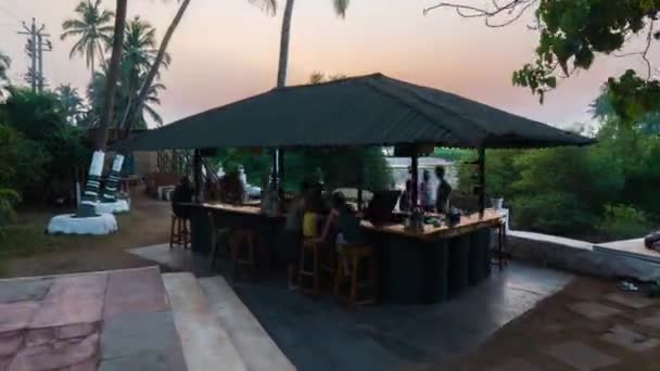 ビーチサイドのレストランカフェバーは、熱帯ゴアの夕日に燃える松明で照らされます。紫の空の下での牧歌的なロマンチックな夏の夜の食事. — ストック動画