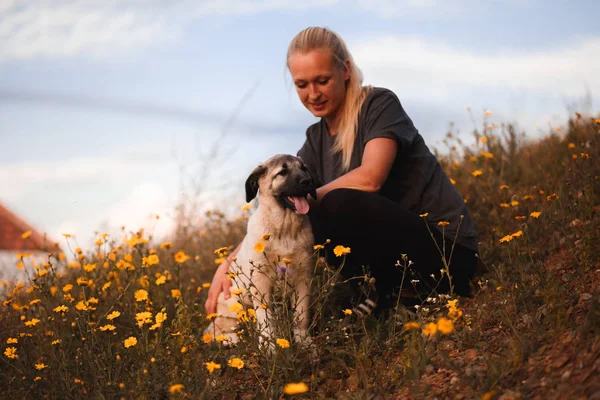 Blondes Mädchen spielt mit Welpe spanische Dogge in einem Feld von gelben Blumen — Stockfoto