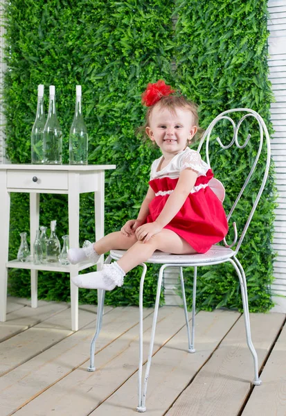Small girl sits at the chair of the green background