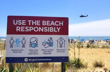 Rehoboth Beach, Delaware, ABD - 13 Haziran 2020 - Tahta kaldırımda yazan tabela ziyaretçilere maske takmalarını, düzenli olarak sterilize olmalarını ve sosyal mesafeyi ölçmelerini tavsiye ediyor.