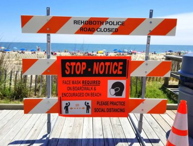 Rehoboth Beach, Delaware, ABD - 13 Haziran 2020 - Tahta kaldırımda yazan tabela ziyaretçilere maske takmalarını ve sosyal mesafe çalışması yapmalarını tavsiye ediyor.
