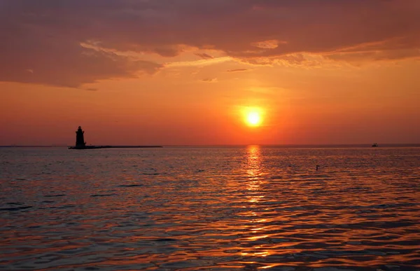 a A distance silhouette of the lighthouse and a boat during sunset at Cape Henlopen State Park, Lewes, Delaware, U.S.A