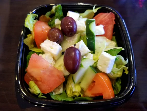 Siyah bir kasenin içinde Yunan salatası, marul, domates, salatalık ve peynir.