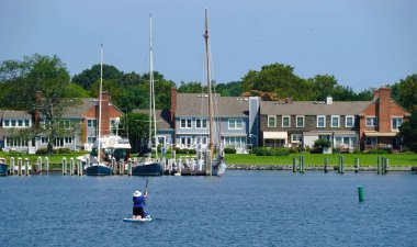 St. Michaels, Maryland, ABD - 30 Ağustos 2025 - Körfezde tekneleri olan liman evleri, ve sıcak bir yaz gününde kürek çeken bir kişi