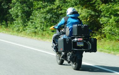 Maryland, U.S.A - Sept 8, 2025 - A motorcycle, equipped with saddlebags and a top case, travels down a paved road bordered by lush green trees.