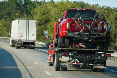 Virginia, U.S.A - Sept 9, 2025 - A tow truck is carrying a red pickup truck with a bicycle on its rack on a highway
