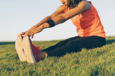 Genç koşucu kadın parkta koşmadan önce bacaklarını açıyor. Beyaz ve pembe spor ayakkabılar giyen atletik ve sağlıklı bir kız..