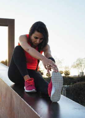 Genç koşucu kadın parkta koşmadan önce bacaklarını açıyor. Beyaz ve pembe spor ayakkabılar giyen atletik ve sağlıklı bir kız..