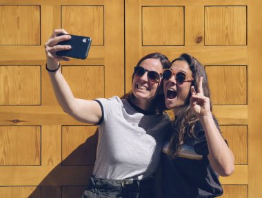 Sarı kapıda selfie için poz veren gülümseyen lezbiyen genç çiftin portresi. Mutluluk ve neşeli yaşam tarzı kavramı.