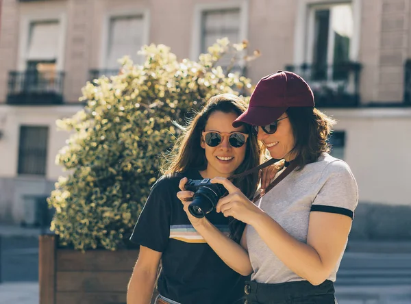 Ein paar schwule Frauen, die zusammen Sightseeing machen, lächelnd seine Reflex-Fotokamera anschauen. gleichgeschlechtliches junges verheiratetes weibliches Paar zeigt etwas Zuneigung lgbt in madrid. — Stockfoto