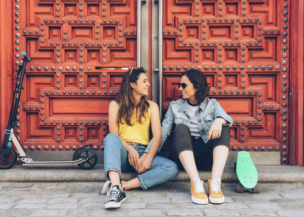 Young lesbian women couple talking and holding hands spending time together, in a red door background. Happiness and relationship concept.
