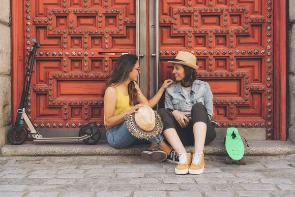 Junge schwule Frauen, die einander vor rotem Türhintergrund anschauen und lächeln. Gleichgeschlechtliches Glück und freudiges Konzept. — Stockfoto