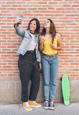 Young women couple making a selfie. Behind brick wall. Positive emotion and tolerance concept.