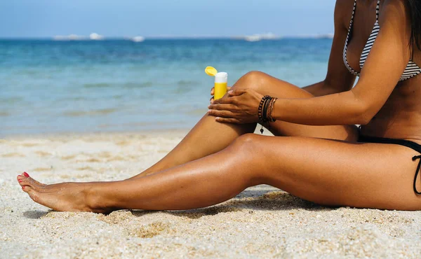 Tanned woman applying sunblock protection in her tanned legs in a paradise beach