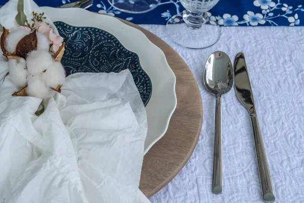 Table Setting - closeup. Interior and decorating ideas with this stack of dinner and salad plates on a blue flowered table cloth, Accented with raw cotton and tiny pink roses. Ready for a garden party, outdoor entertaining, brunch or special event.