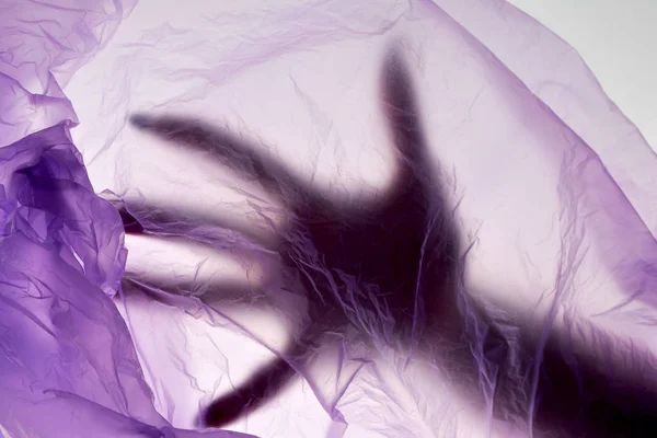 Plastik torbadaki ölü el. Cinayet konsepti. Puple renk arka plan.