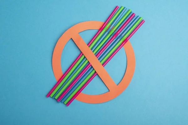 No plastic. A lot of colorful plastic straw set up in a red prohibition circle over a blue background, telling a campaign of ban on it for an environmental concept. Copy space for text.