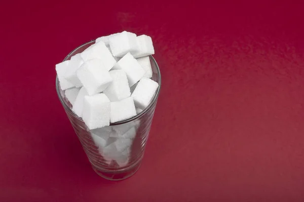 La presencia de una gran cantidad de azúcar en un vaso de refresco. Vista superior. Cubos de azúcar jn el vidrio sobre fondo rojo. Copiar espacio para texto . — Foto de Stock