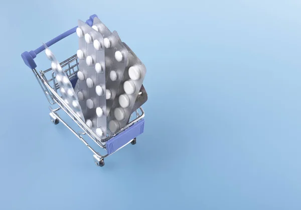 Pills in cart. Shopping cart loaded with pills on light blue background. The concept of medicine. Copy space.