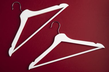 Kırmızı arka plan üzerinde boş beyaz ahşap giysi askıları, üst görünümü. Düz yatıyordu