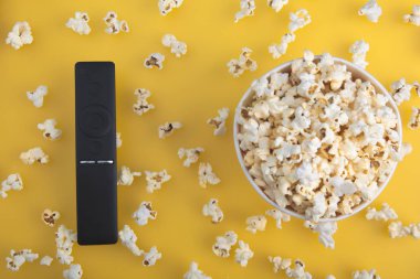 Sarı bir arka plan üzerinde patlamış mısır ve Tv uzaktan bir kağıt fincan. Tv, film, dizi, spor, dizi izleme konsepti. Düz döşeme, üst görünüm.
