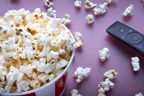 Close-up of remote control and striped bowl of popcorn on red background. The concept of watching a movie, TV, DVD. Entertainments