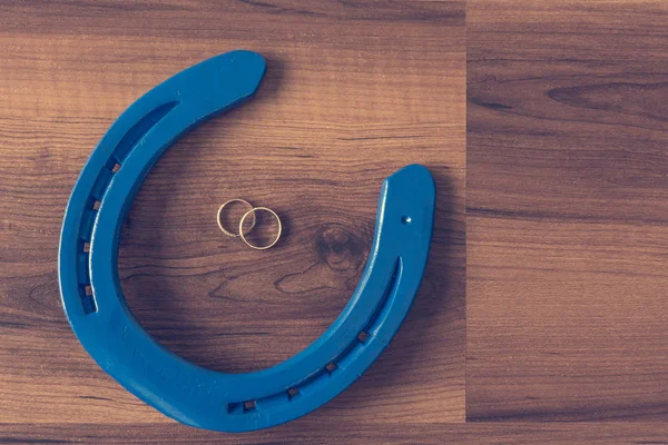 Wedding rings in blue horseshoe on wooden desk. — Stock Photo, Image