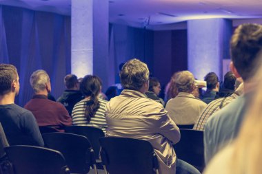 İnsanlar kapalı konferansta sunum dinlerken.