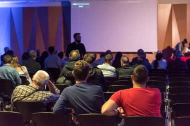 İnsanlar kapalı konferansta sunum dinlerken.