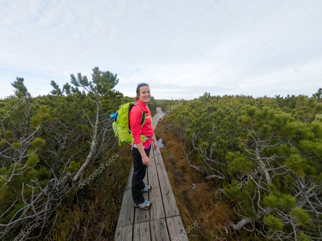 Female hiker walking on a wooden boardwalk across marshes.