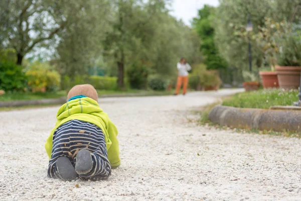 Visão traseira de um bebê rastejando em direção a sua mãe ao ar livre . — Fotografia de Stock
