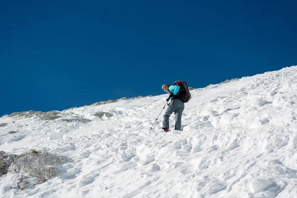 Female alpinist ascending a steep snowy slope. — Stock Photo, Image
