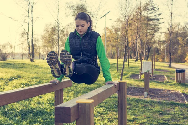 Athletic female doing leg raises on wooden beams outdoor. — Stock Photo, Image