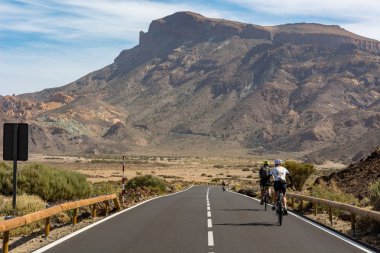 Cyclist cycling on a road through volcanic landscape. clipart